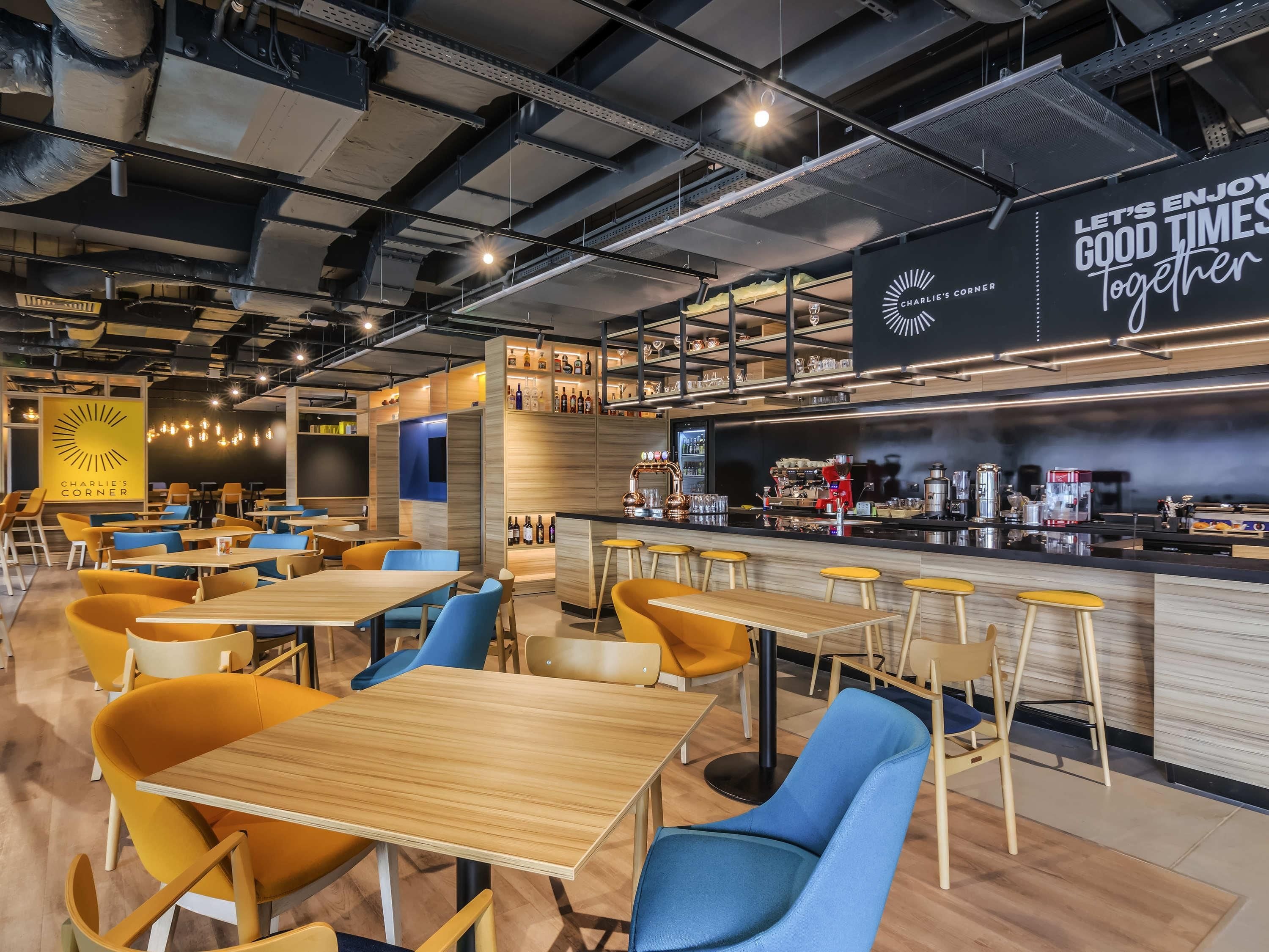 L’intérieur d’un café moderne, avec des tables et des chaises en bois, un bar et une enseigne sur laquelle on peut lire : « PASSONS DE BONS MOMENTS ENSEMBLE ».