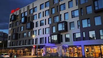Un bâtiment d'hôtel moderne, avec une enseigne « IBIS HOTEL » bien visible, de nombreuses fenêtres et un hall d'entrée bien éclairé.