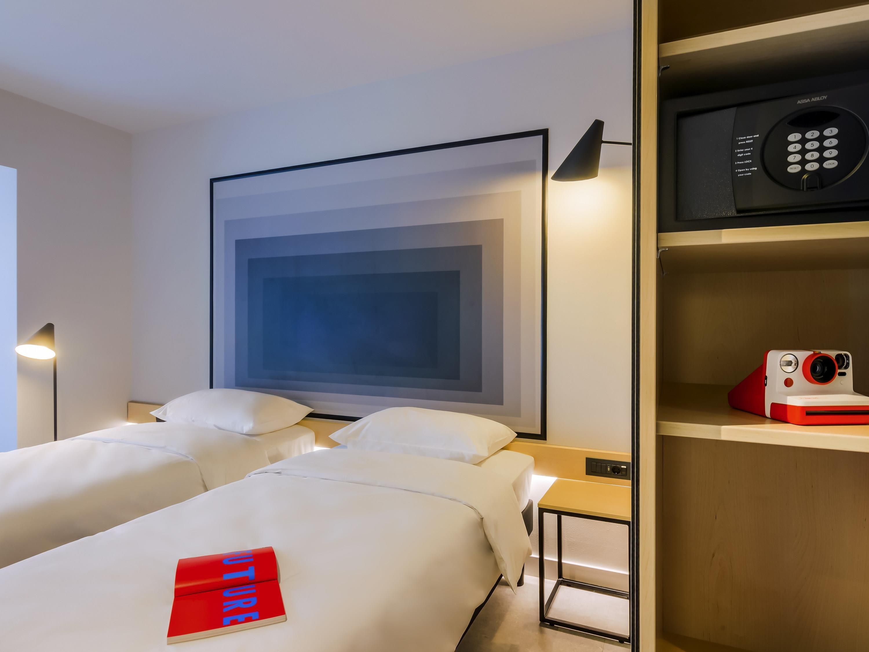 A hotel room with two beds, a large abstract painting on the wall, a modern lamp, a microwave, and a red book on one of the beds.