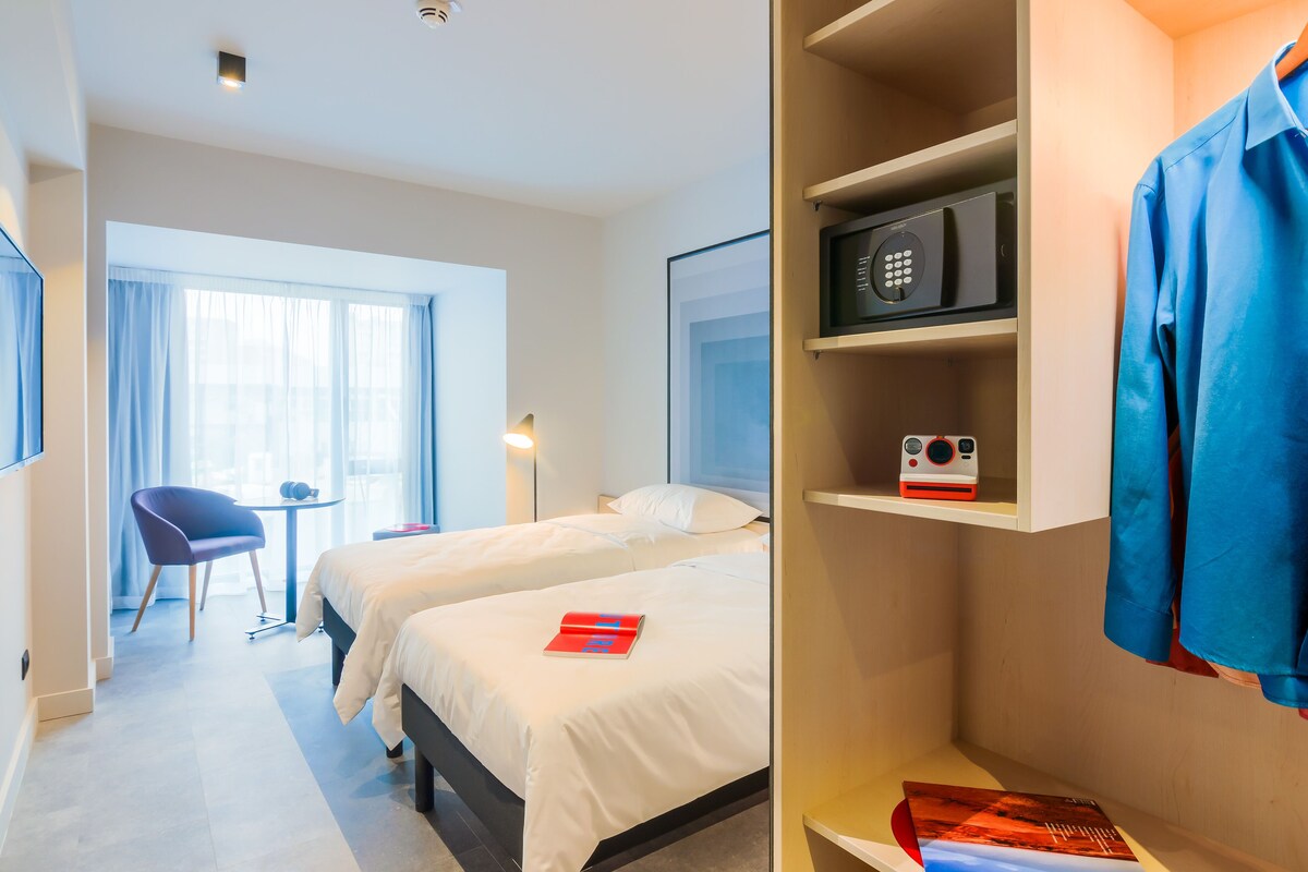 Una habitación de hotel con dos camas, un escritorio, una silla y un armario.