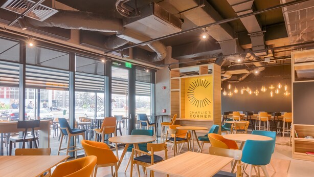 Un café moderno con mesas y sillas, ventanas amplias y un letrero que dice 'CHARLIE'S CORNER'.
