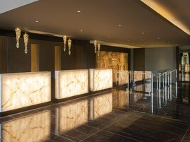 Un vestíbulo moderno con mostradores de recepción de mármol, una escalera y lámparas decorativas colgantes.