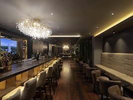 A bar area with a long counter, multiple bar stools, and a large chandelier.