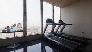 Een moderne sportschool met een loopband, een glazen tafel met fitnessartikelen en een stadszicht door grote ramen.