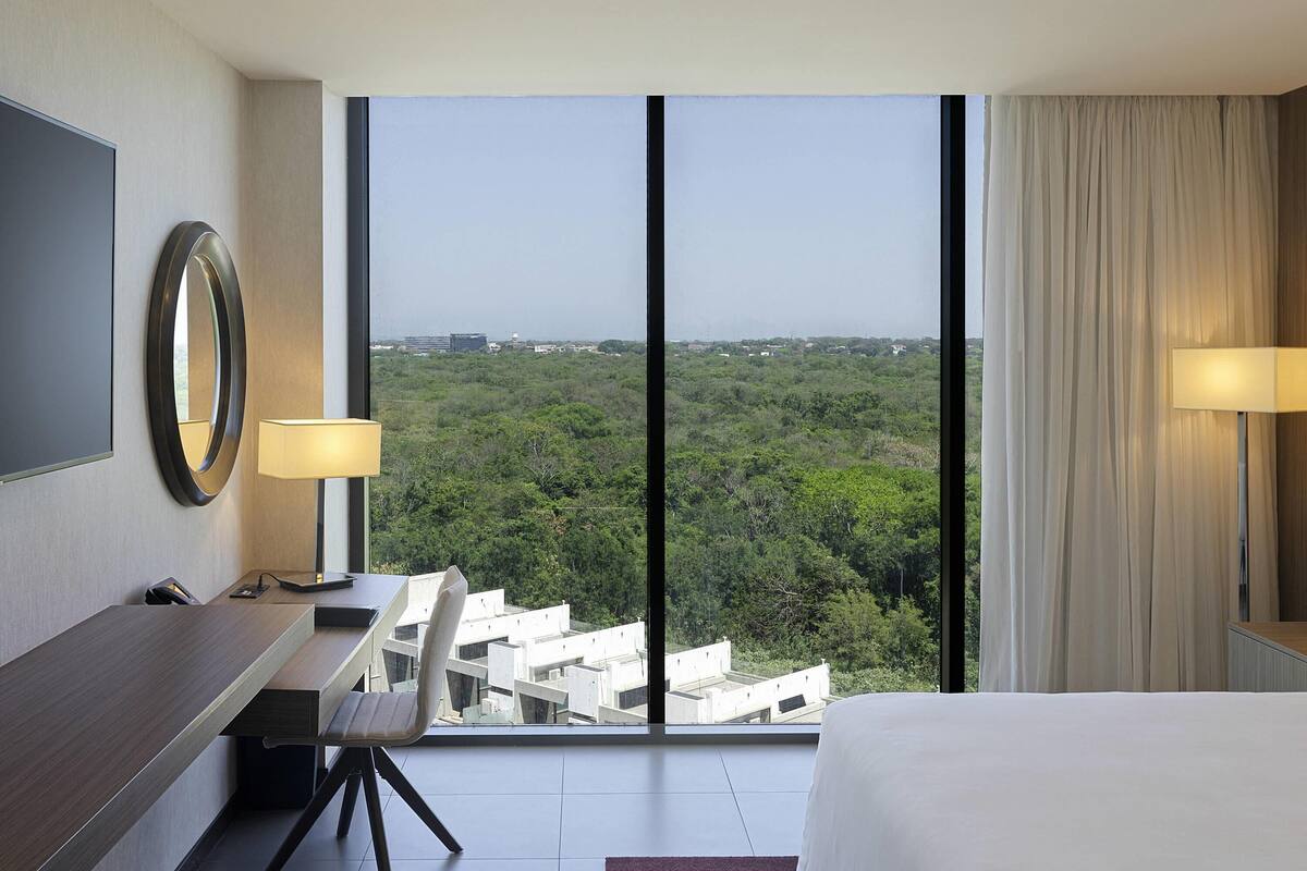 Ein Hotelzimmer mit großem Fenster, Schreibtisch, Stuhl, Bett und Fernseher.