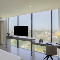 A hotel room with a large window, a bed, a desk with a telephone, and a television.