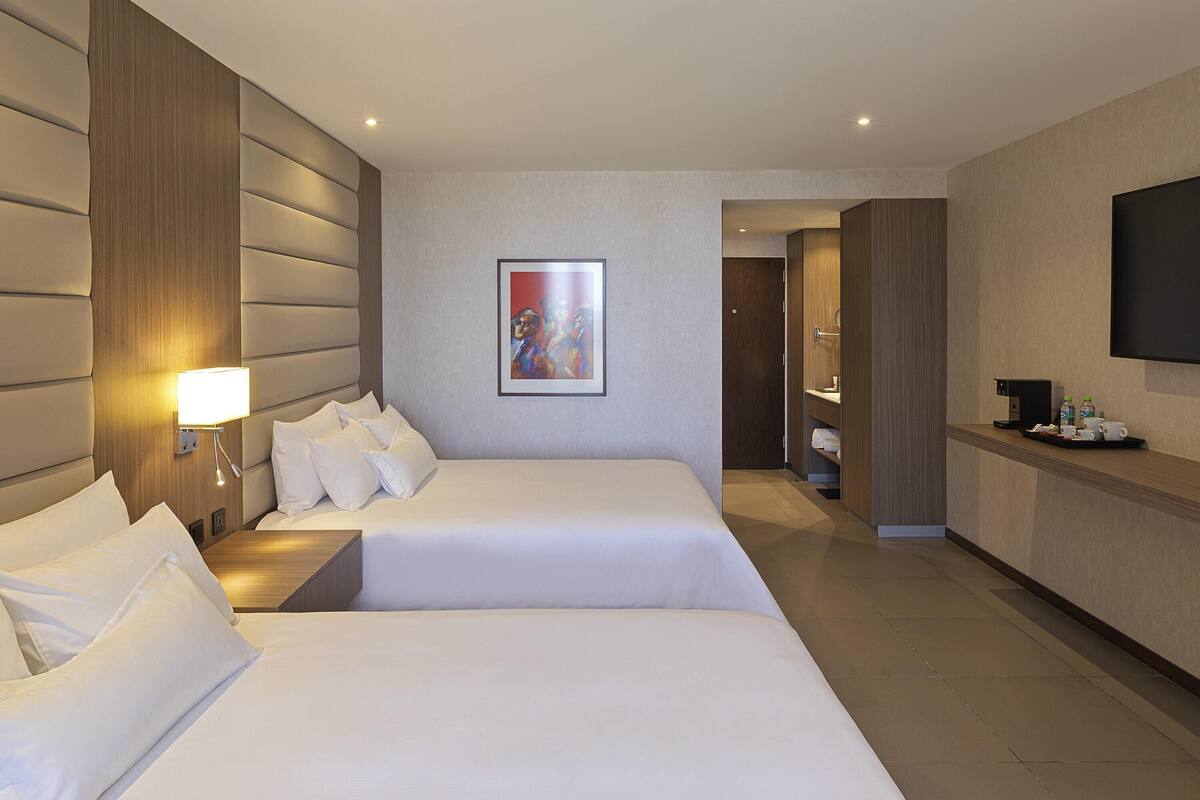 Ein Hotelzimmer mit zwei Betten, einem Bild an der Wand, einem Fernseher und einem Schreibtisch mit Kaffeemaschine.