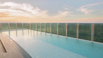 Una piscina infinita rectangular con agua azul cristalina, rodeada de paneles de vidrio y una terraza de madera.