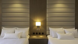 Une chambre d’hôtel avec deux lits, une table de chevet et une lampe fixée au mur.