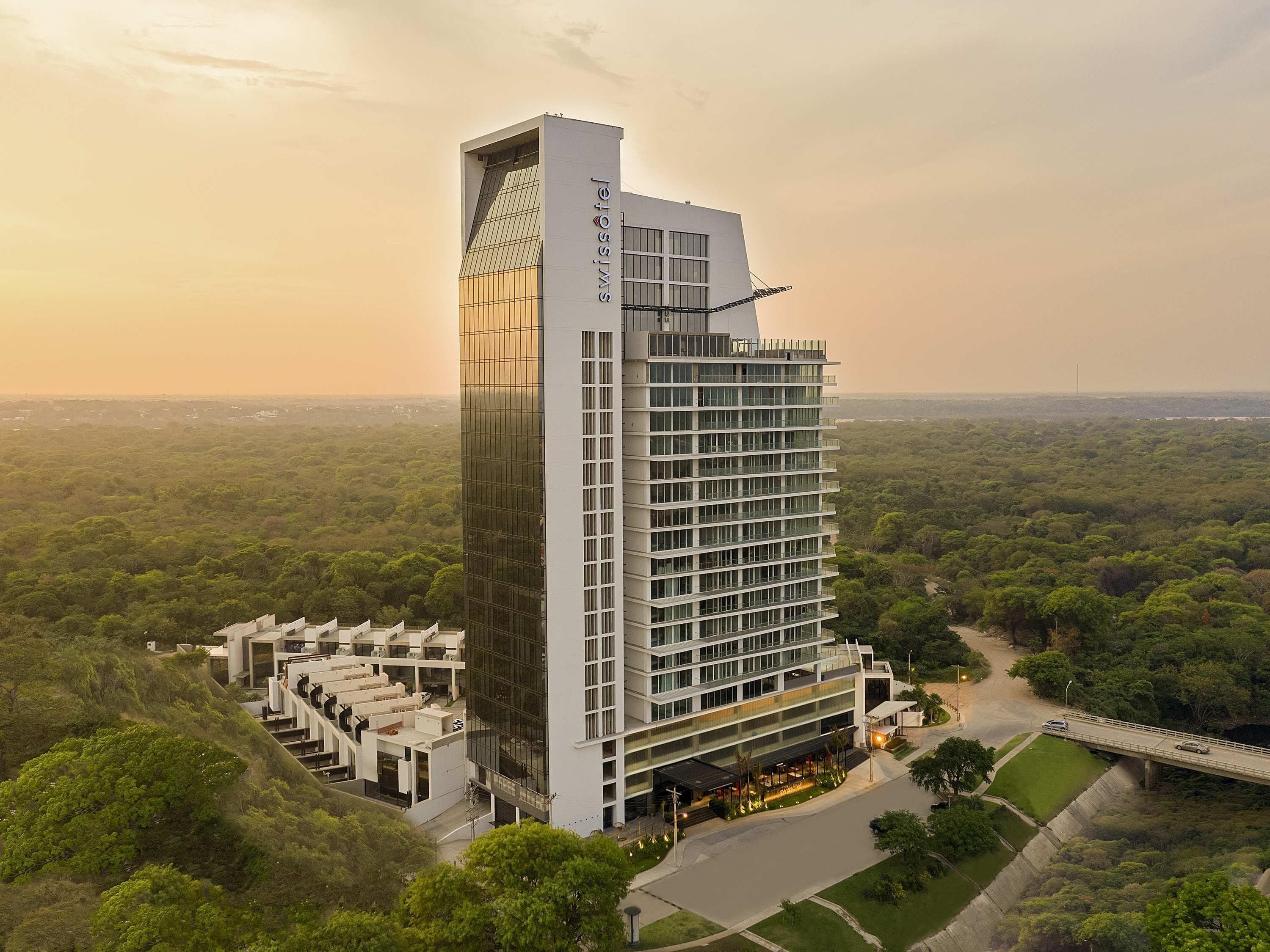 Un hôtel moderne doté d’une haute tour, de nombreux étages et entouré d’un paysage verdoyant luxuriant.