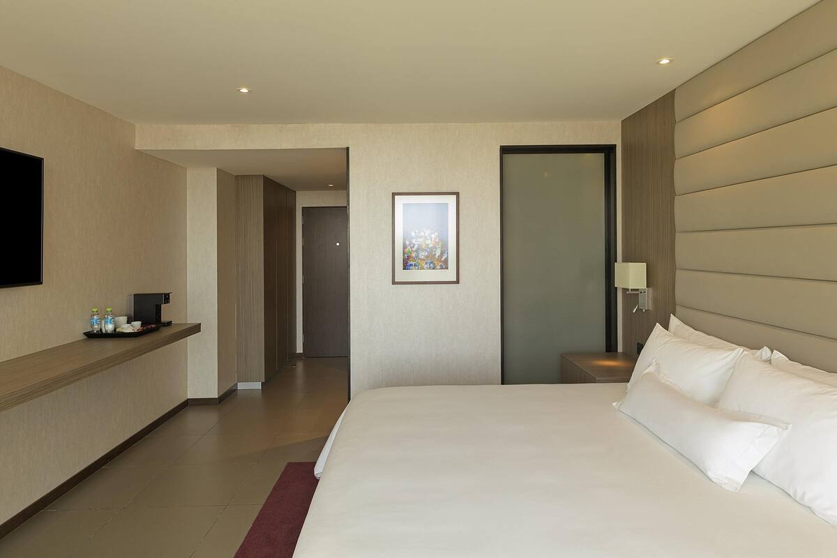 Ein Hotelzimmer mit Bett, Fernseher, Kaffeeautomat und einem Bild an der Wand.