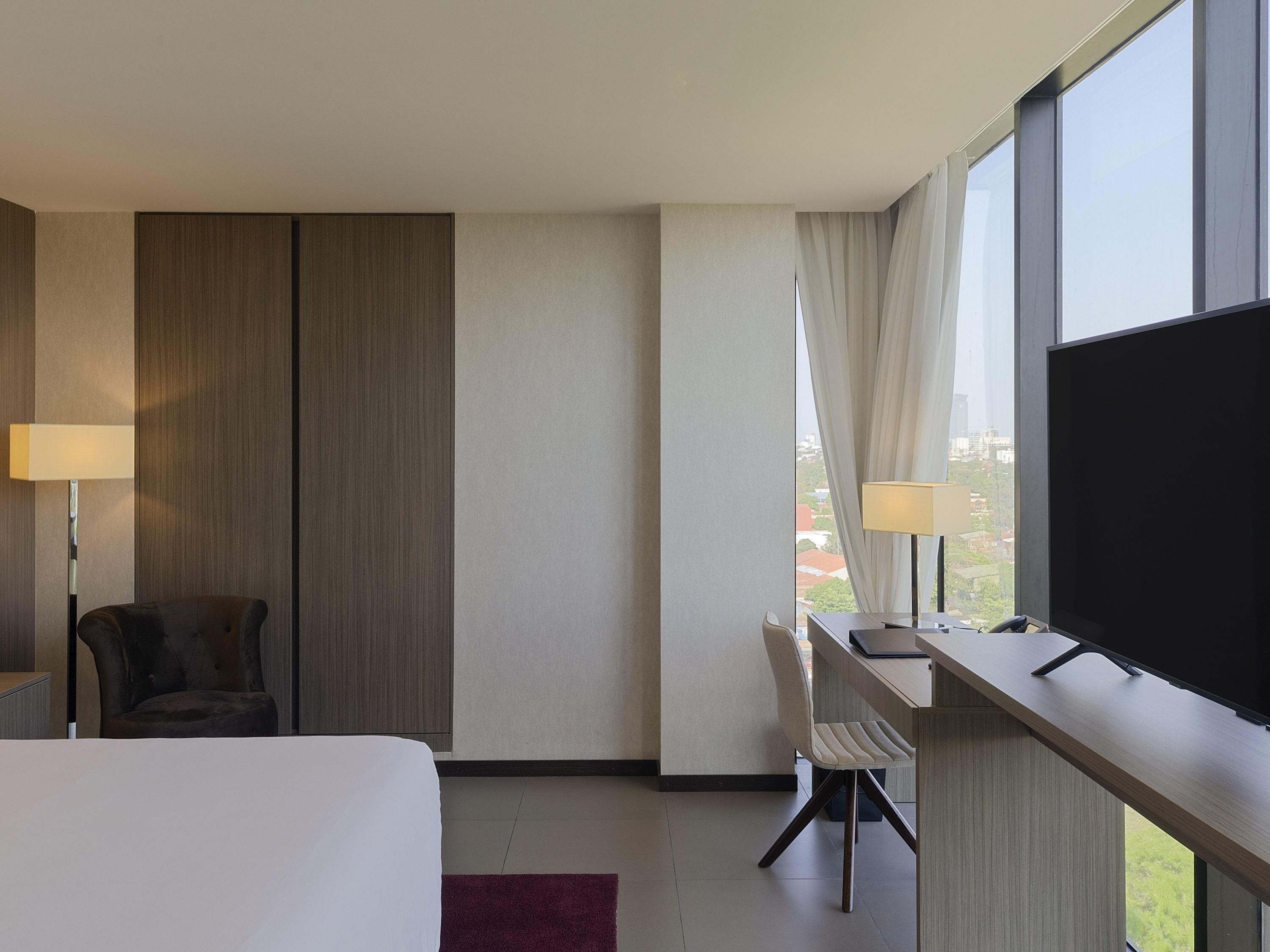 A hotel room with a bed, a desk, a chair, a TV, and a window with curtains.