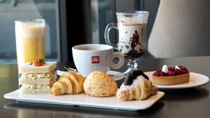 Een tafel met diverse gebakjes, een kop koffie en een nagerechtenbord.