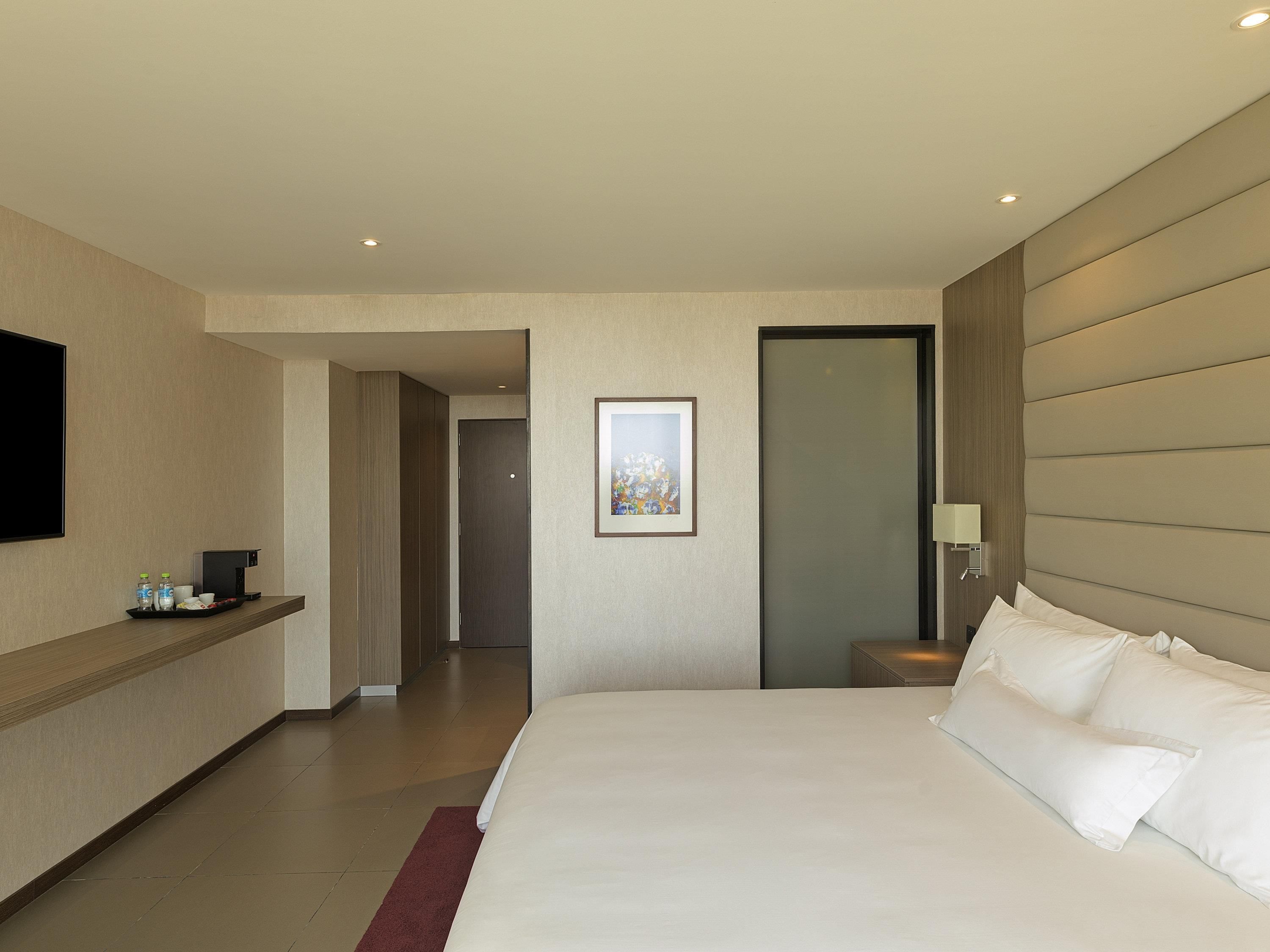 A hotel room with a bed, a TV, a coffee machine, and a painting on the wall.