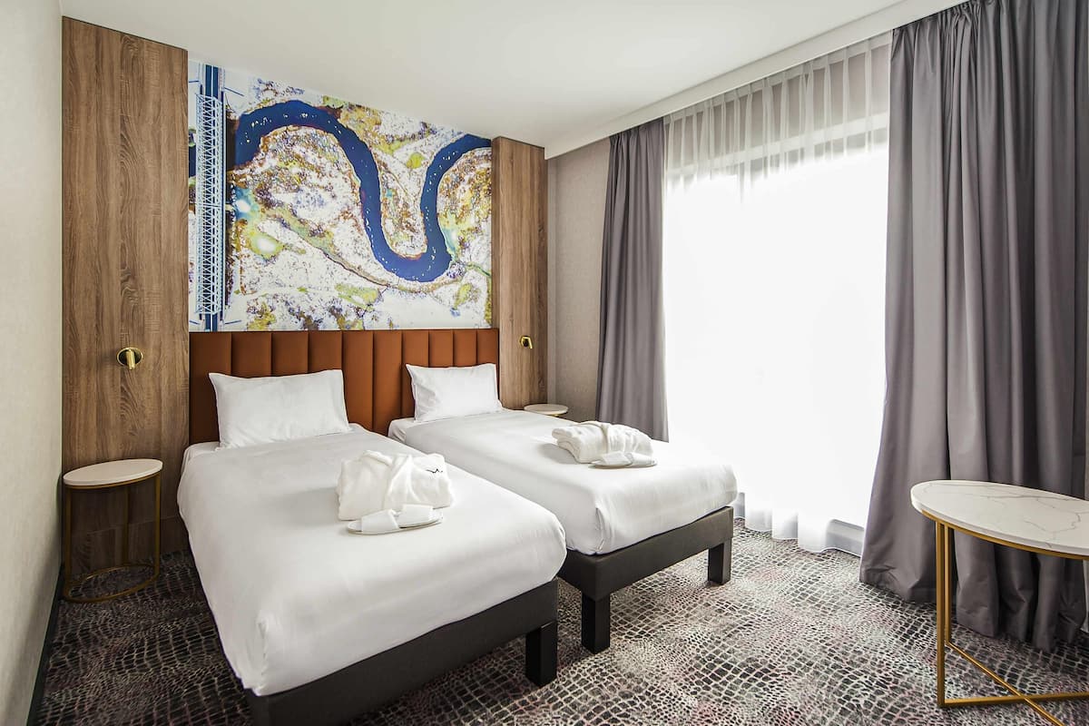 Une chambre d’hôtel avec deux lits, une grande peinture abstraite au mur, une table ronde et une moquette à motifs.