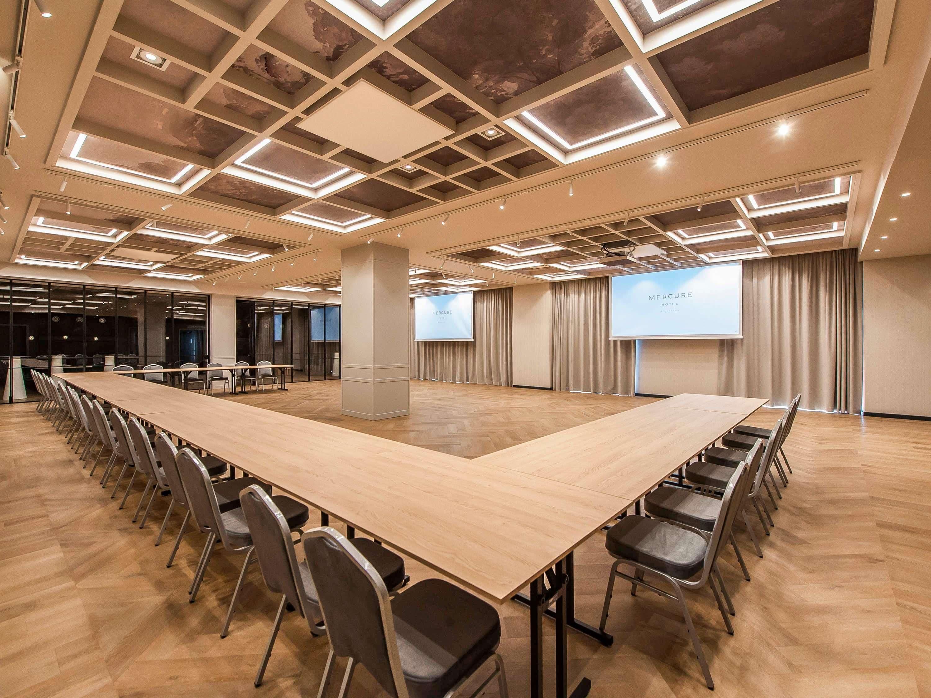 Une salle de conférence équipée d’une longue table, de chaises, d’un écran de projection et d’un plafond doté d’un éclairage encastré.