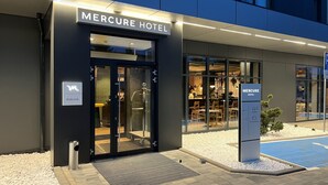 Exterior del hotel Mercure con entrada de vidrio, interior de restaurante visible y cartel que indica servicios como estacionamiento y restaurante.