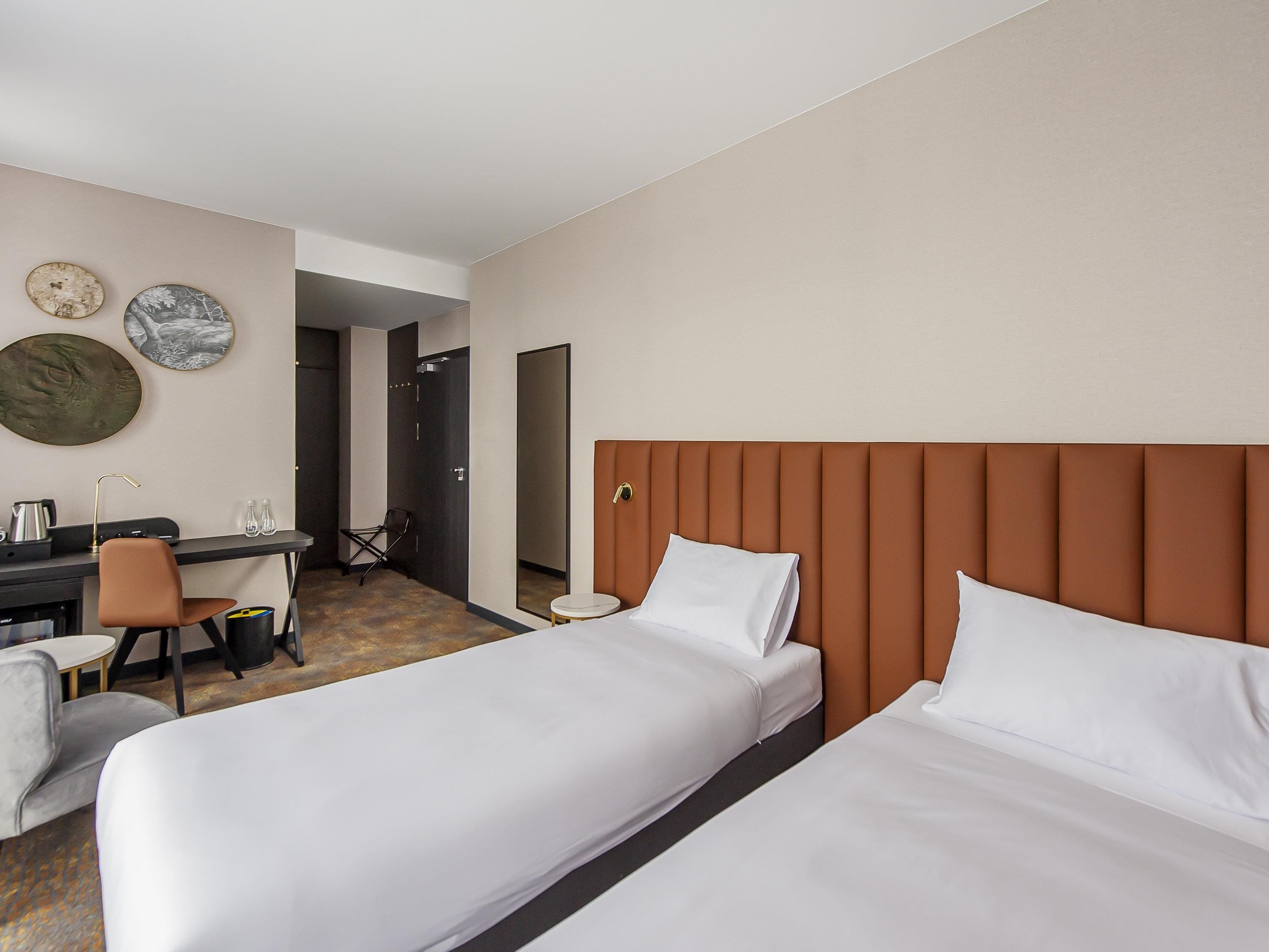 A hotel room with two beds, a desk with a chair, and a small table.