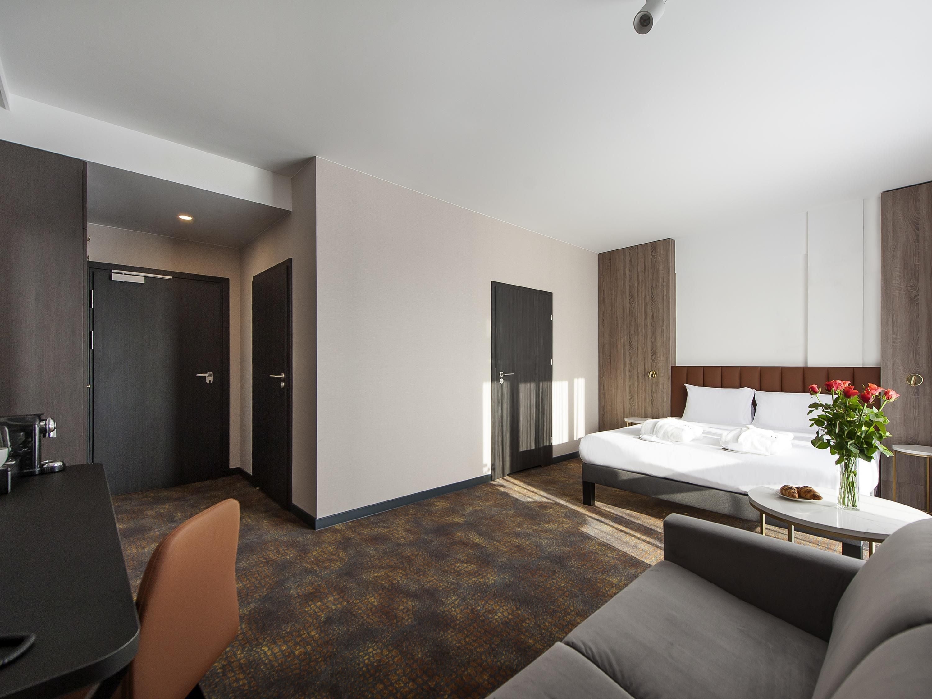 A modern hotel room with a bed, a desk, and a sofa.