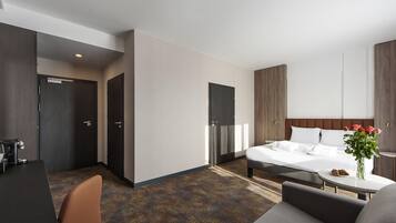 A modern hotel room with a bed, a desk, and a sofa.