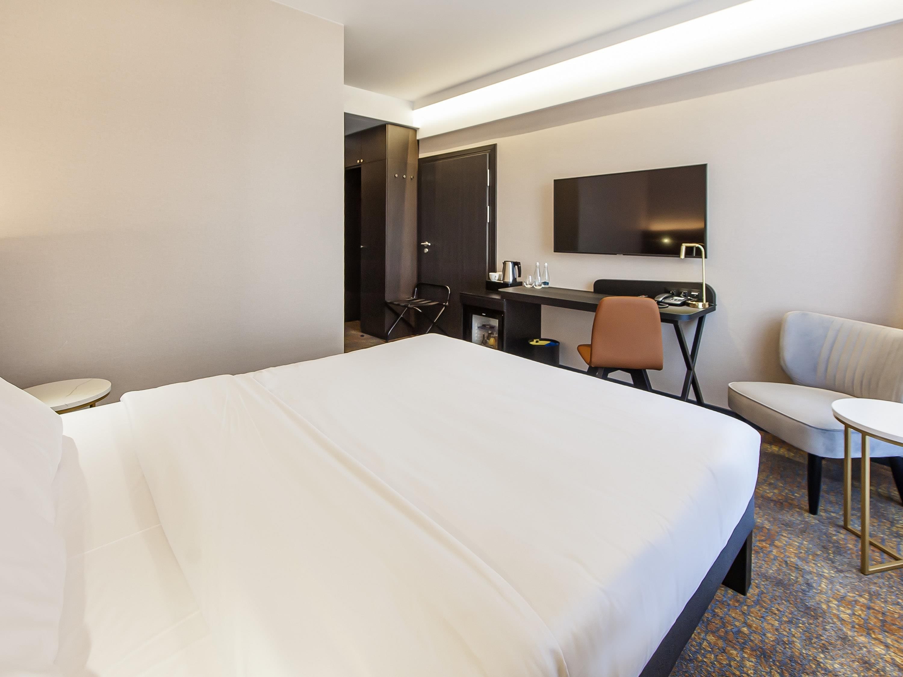 Una habitación de hotel con una cama grande, un escritorio, una silla, un sofá y un televisor.