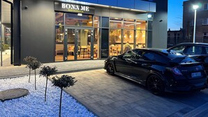 Un edificio moderno con un restaurante llamado "BONAME" y un coche negro estacionado adelante.