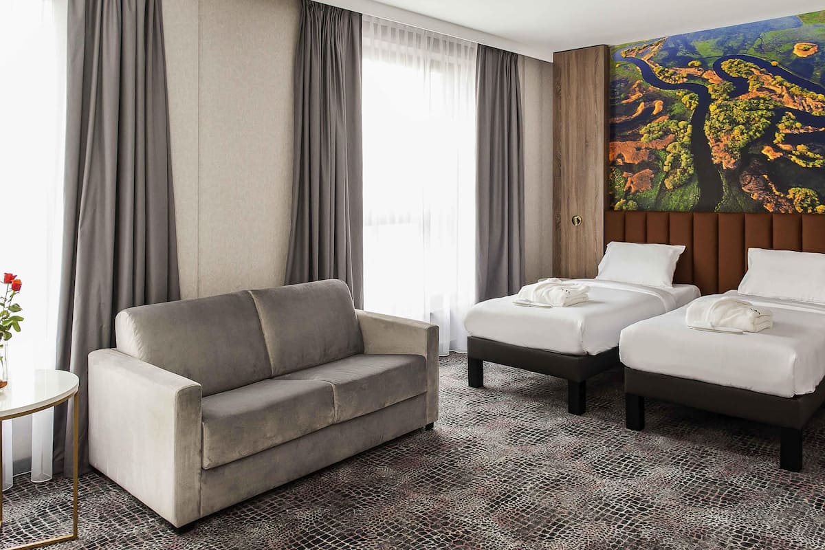 Une chambre d’hôtel avec un canapé, deux lits, un tableau et une moquette à motifs.