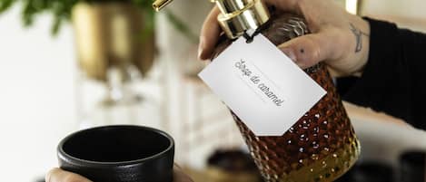 Une main tenant une bouteille dont l’étiquette indique « sirop de canne à sucre » et une tasse noire.