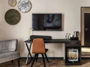 A modern hotel room with a flat-screen TV mounted on the wall, a desk with a chair, a sofa, and a minibar. - Mercure Bialystok (Bialystok)