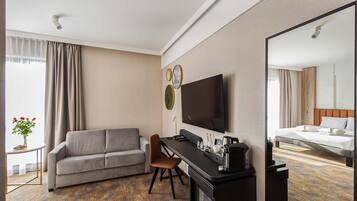 A hotel room with a sofa, a desk with a flat-screen TV, a bed, and a mirror.