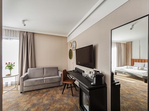 Een hotelkamer met een slaapbank, een bureau met een flatscreen-televisie, een bed en een spiegel.