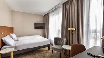 Quarto de hotel com cama, uma cadeira, escrivaninha, televisão e abajur.