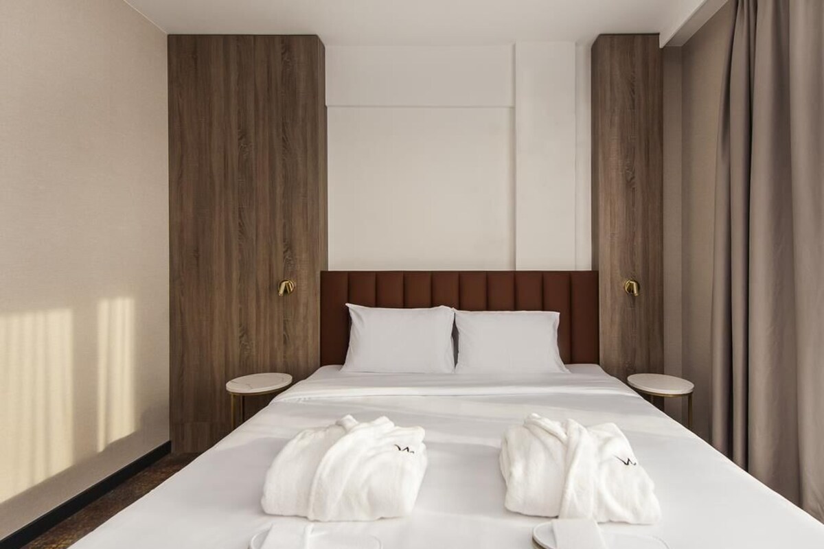A hotel room with a large bed, wooden panel walls, two bedside tables, and a view of the outdoors.