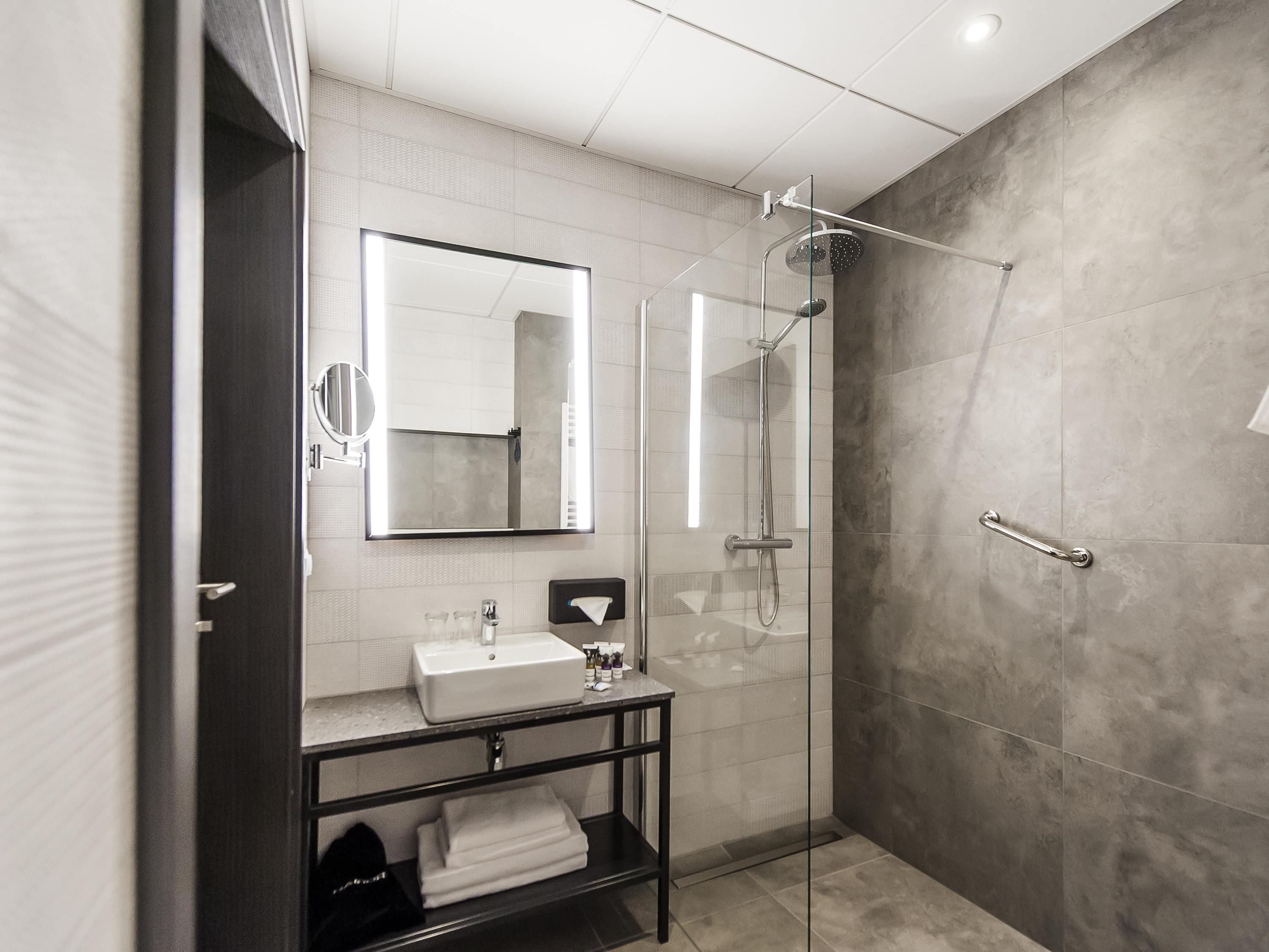 Une salle de bain moderne dotée d’une douche à parois de verre, d’un grand miroir et d’un meuble-lavabo avec un évier et un porte-serviettes.