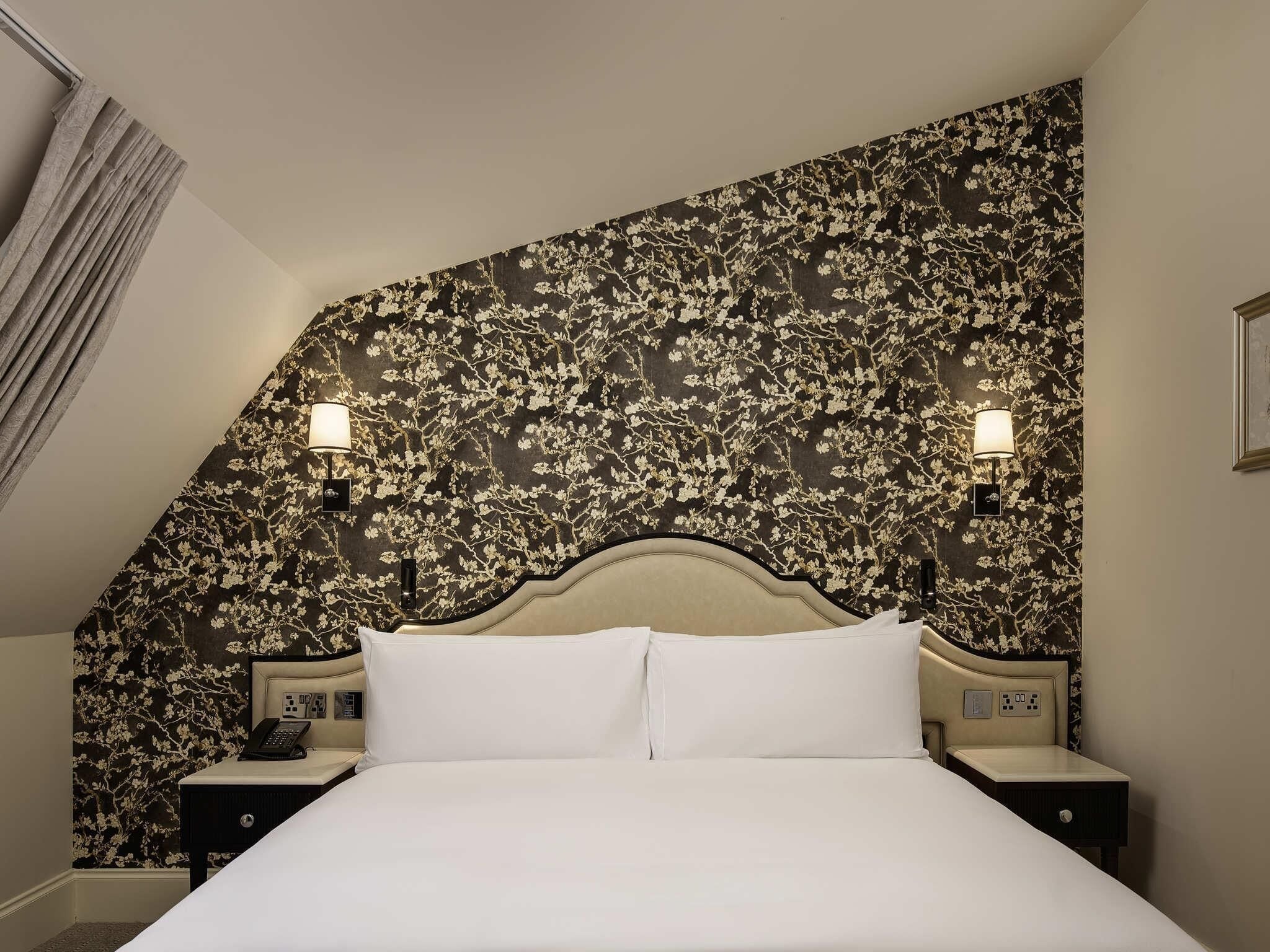 A hotel room with a large bed, two bedside tables, a wall-mounted telephone, and two wall-mounted lamps.