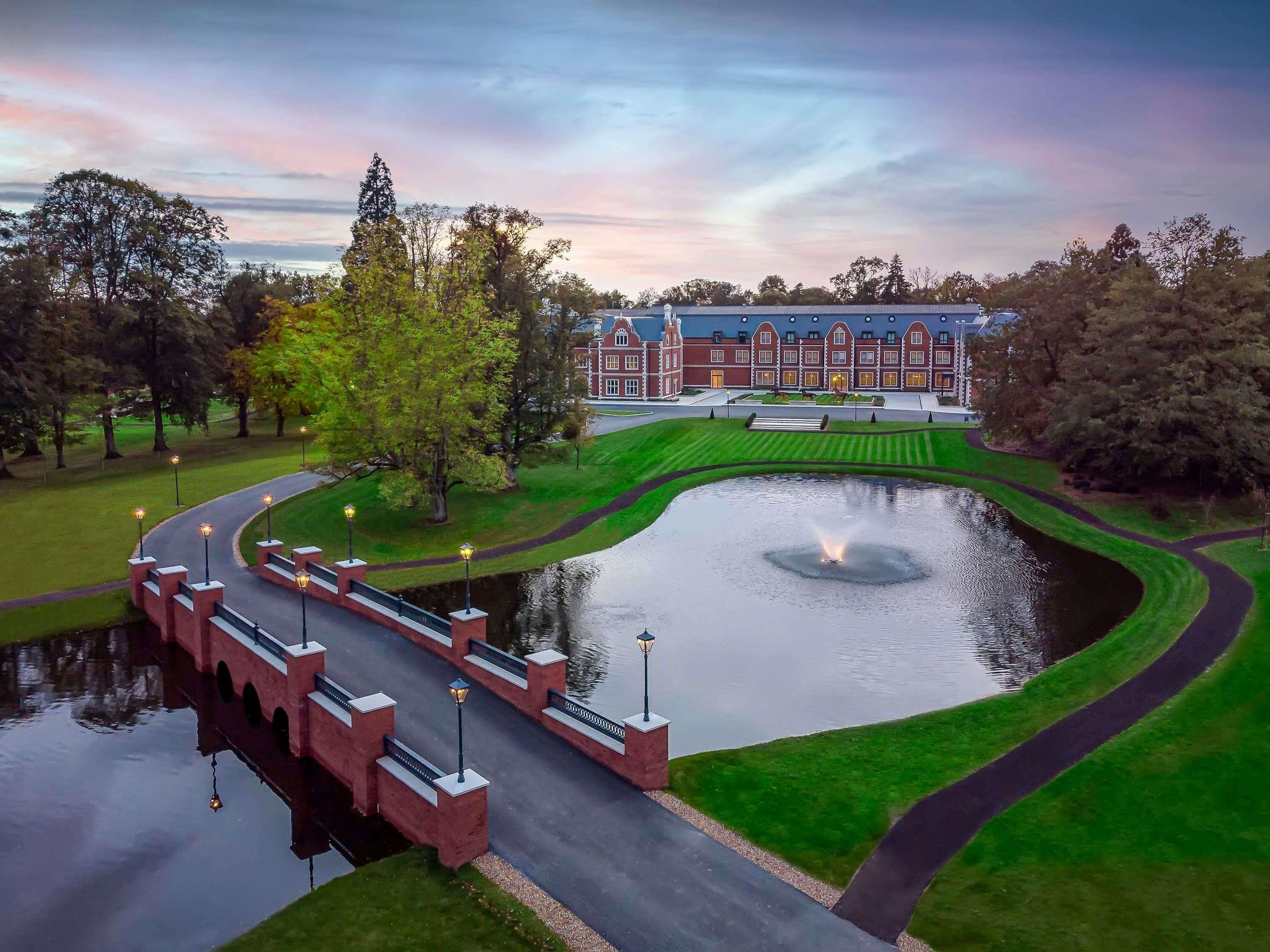 A landscaped area with a pond, a bridge, and a building with a red facade.