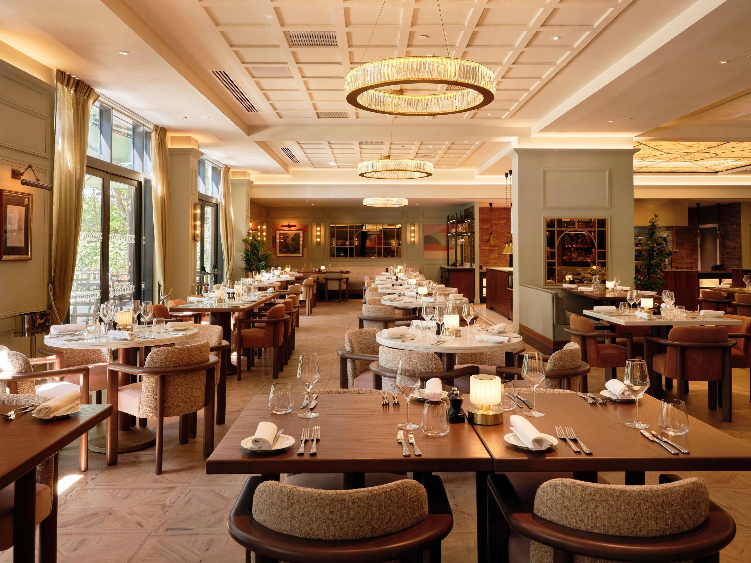A restaurant with multiple dining tables, chairs, and chandeliers.