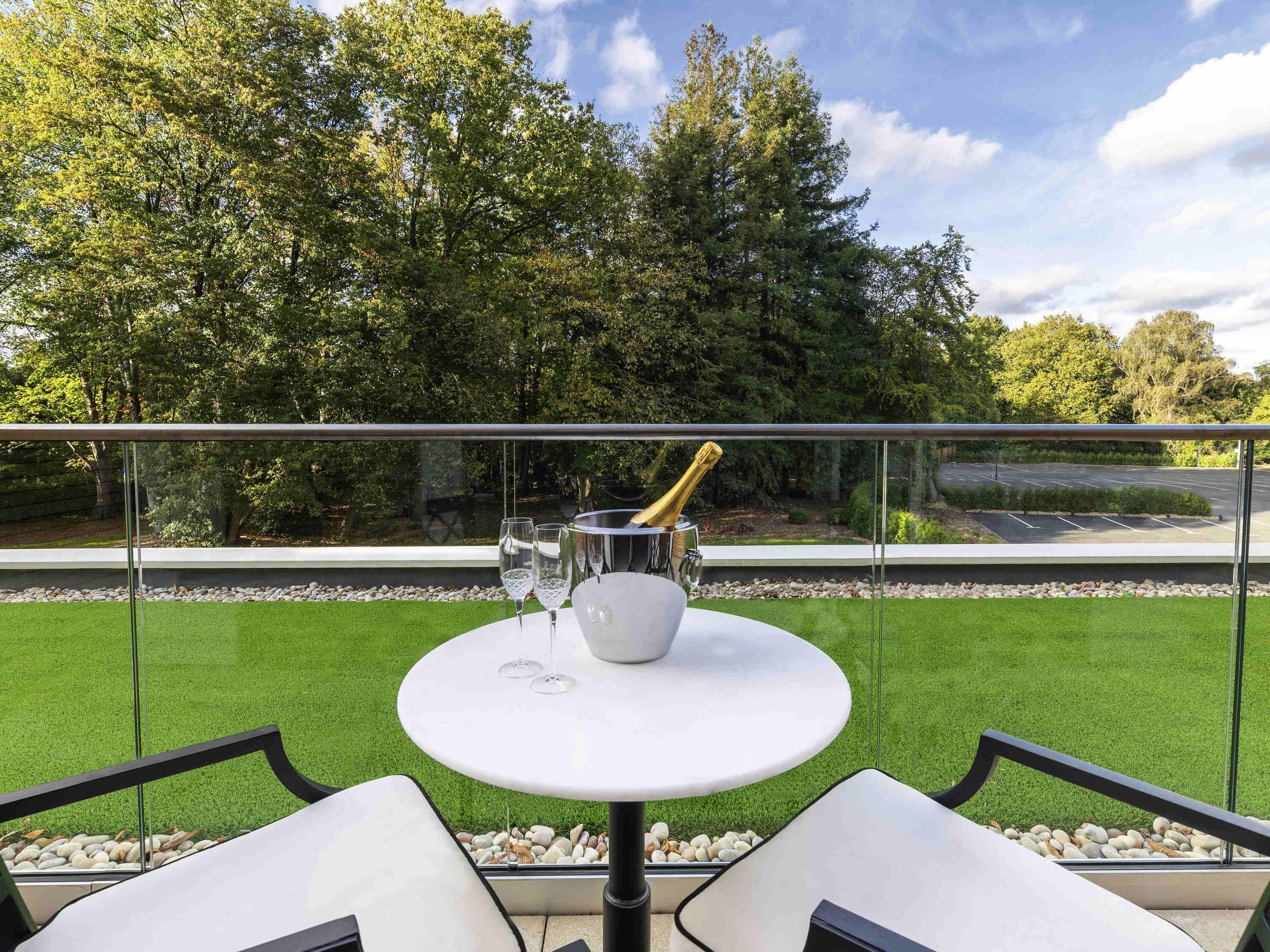 A balcony with a round table, two chairs, a champagne bottle, and glasses.
