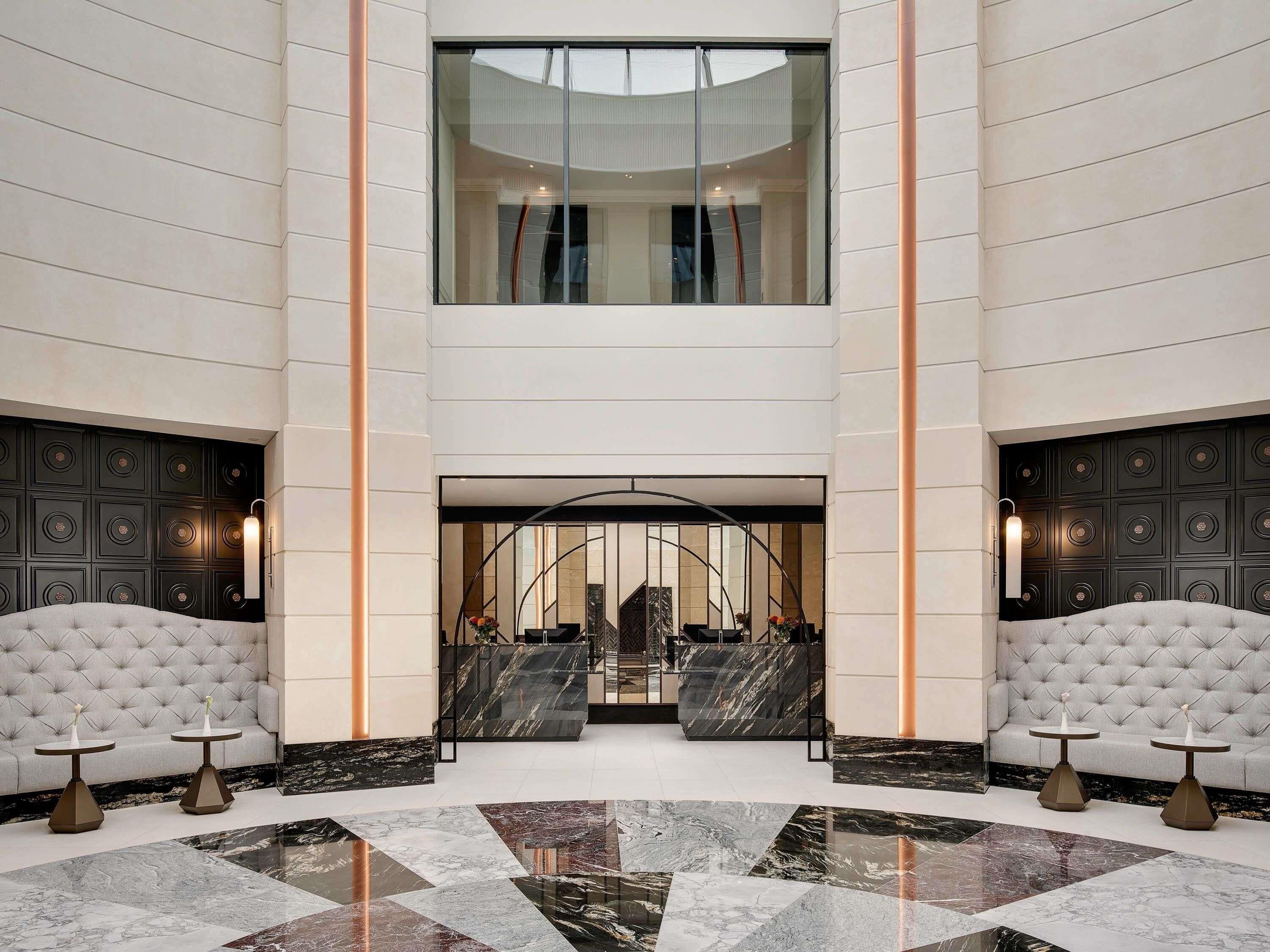 A spacious lobby with a high ceiling, marble flooring, and a central seating area with a curved bench.