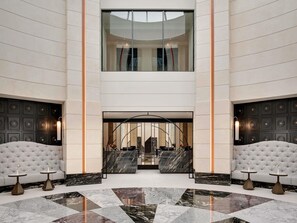 Un vestíbulo amplio con techo alto, piso de mármol y una zona de estar central con un banco curvo.