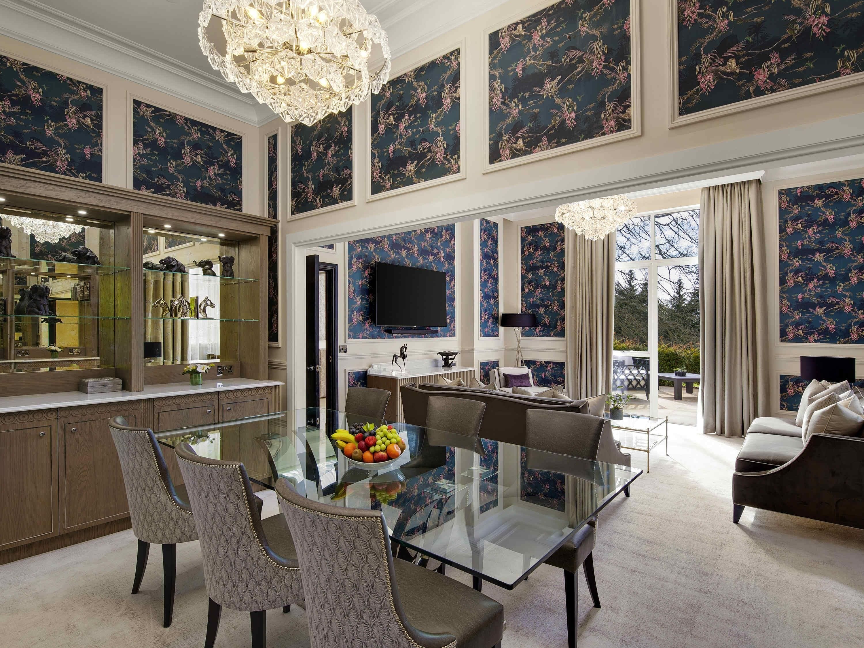 Un amplio comedor con una mesa y sillas de vidrio, una lámpara de araña grande y vistas al exterior.