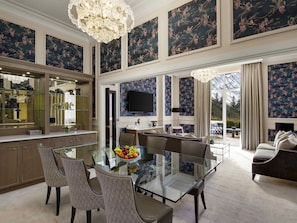 Uma ampla sala de jantar com uma mesa e cadeiras de vidro, um grande lustre e vista para o exterior.