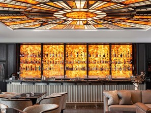 A bar area with a unique ceiling design and a wall of illuminated bottles. - Fairmont Windsor Park (Egham)