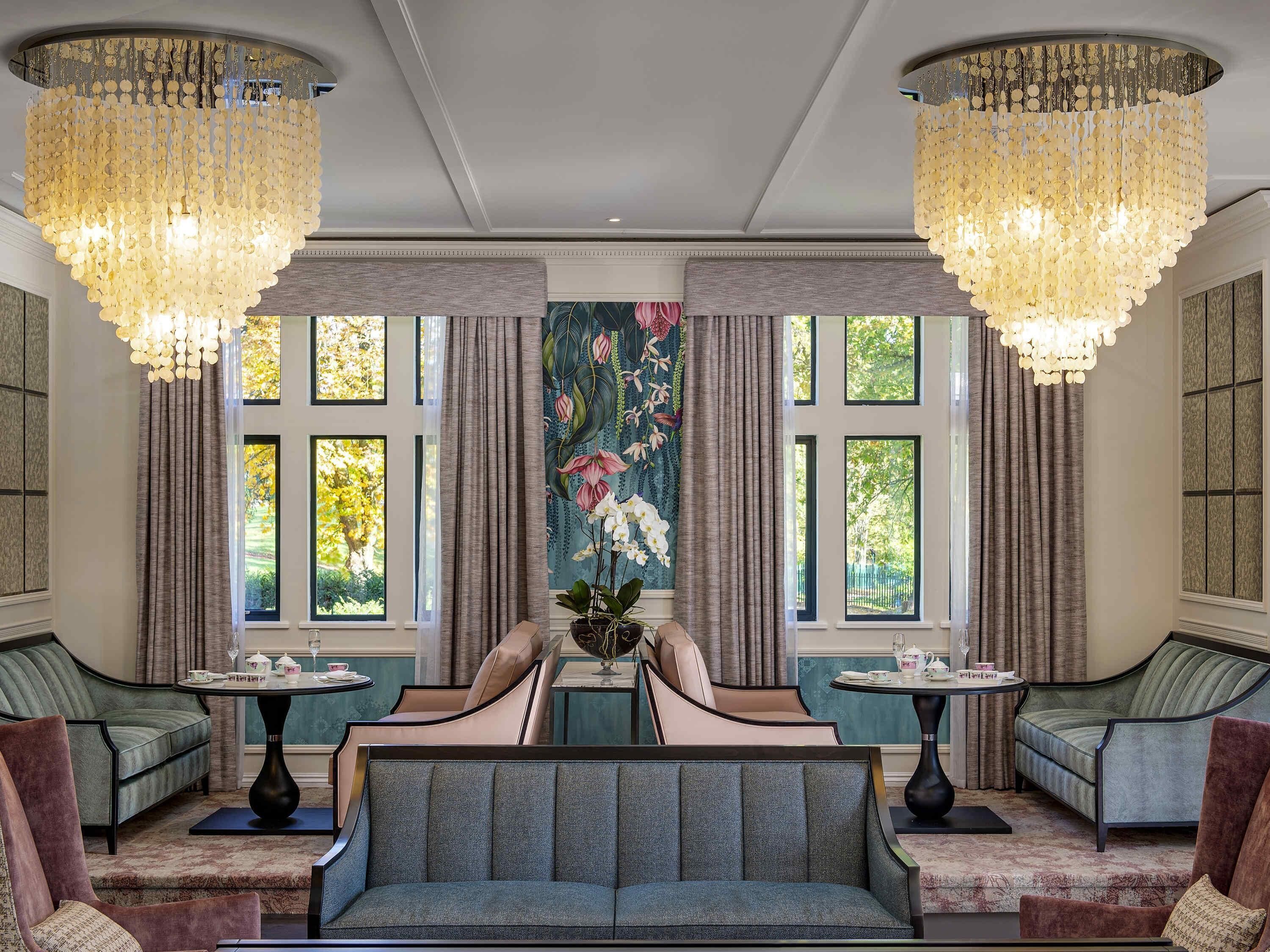 A luxurious room with a large sofa, two armchairs, a table with teacups, and a floral tapestry.