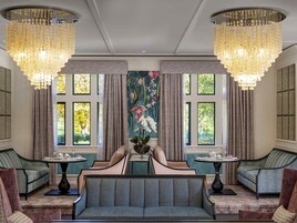 A luxurious room with a large sofa, two armchairs, a table with teacups, and a floral tapestry.