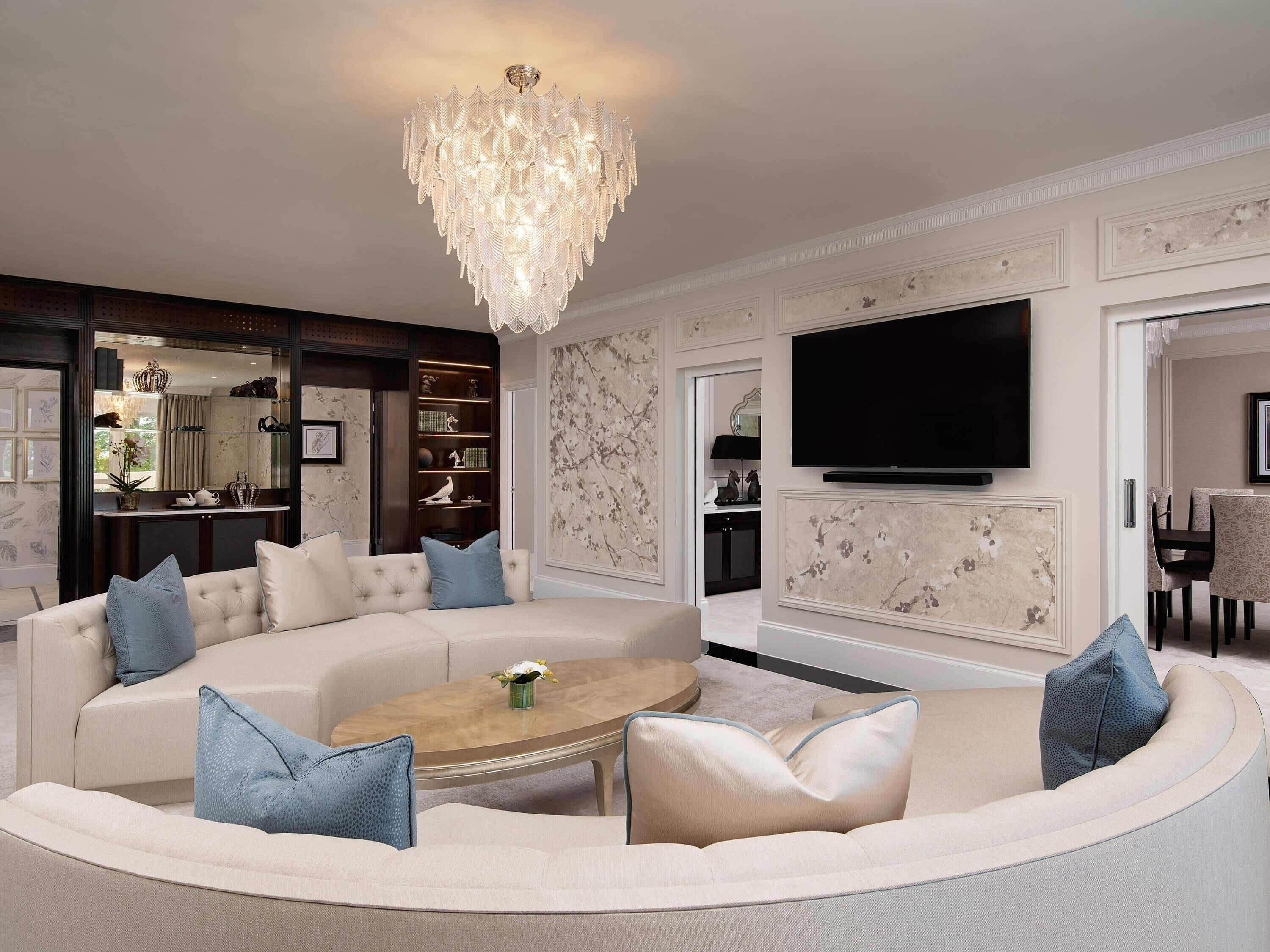 A modern living room with a large sofa, a coffee table, a chandelier, and a flat-screen TV.