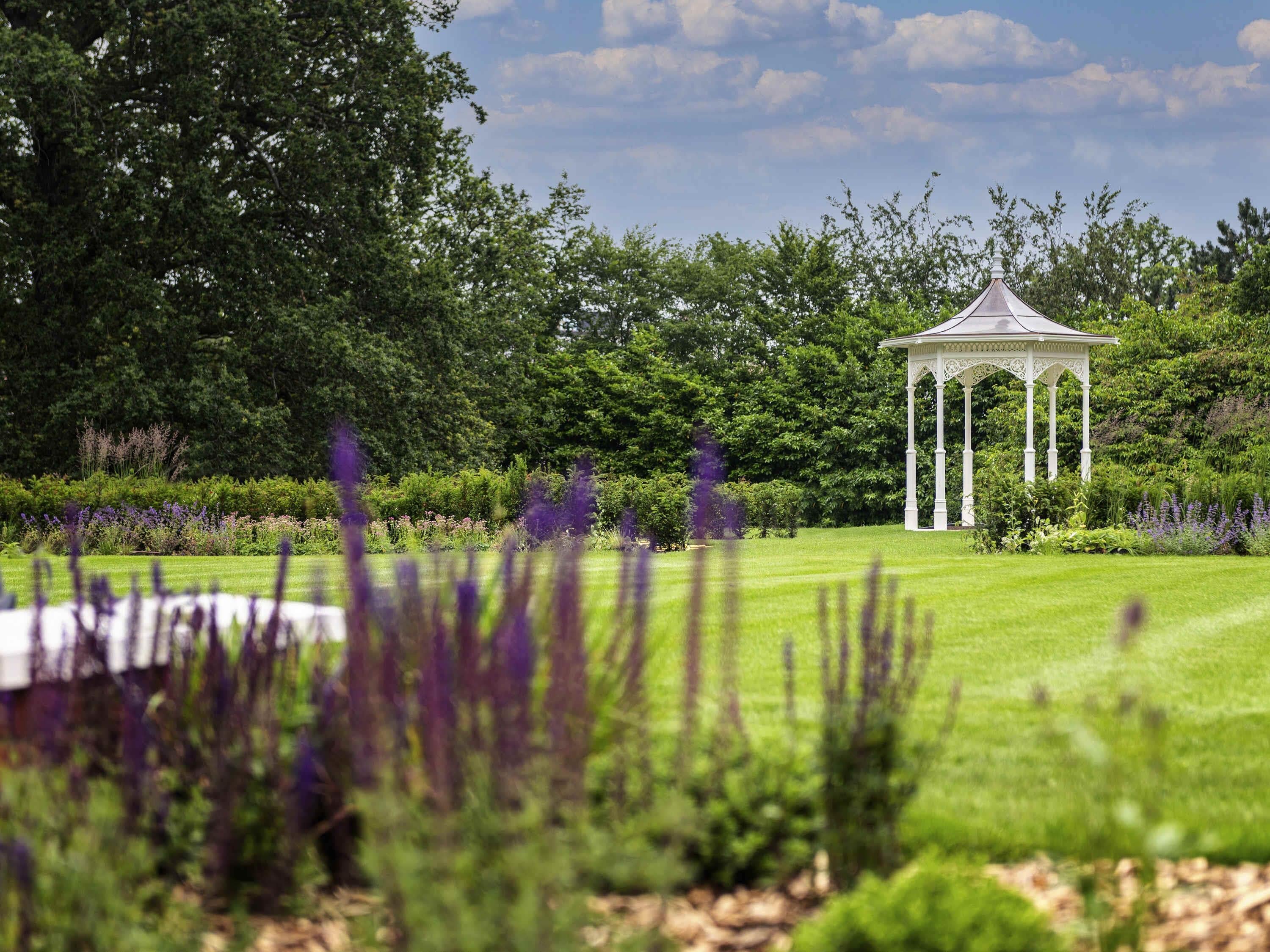 A gazebo in a lush garden with dense trees in the background.