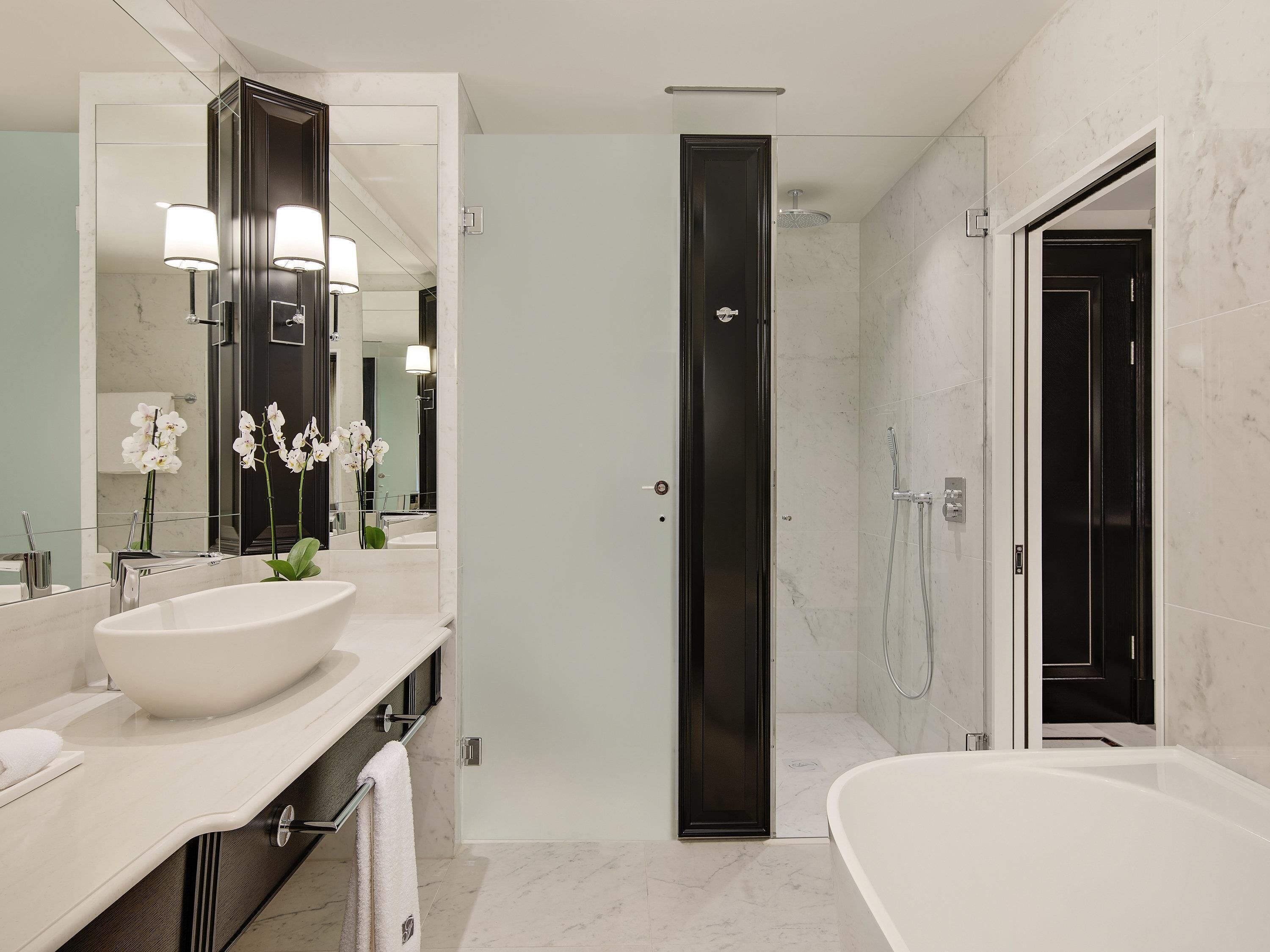 A modern bathroom with a large mirror, two sinks, a bathtub, and a shower.
