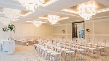 A spacious hall with rows of white chairs, a chandelier, and a large door.