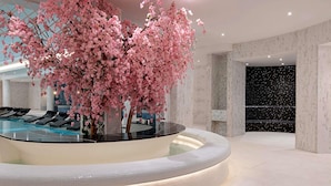A modern indoor pool area with a central cherry blossom tree, lounge chairs, and a marble wall with a starry pattern. - Fairmont Windsor Park (Egham)
